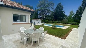 A patio area with a round table and white chairs, a swimming pool, and a well-maintained lawn.