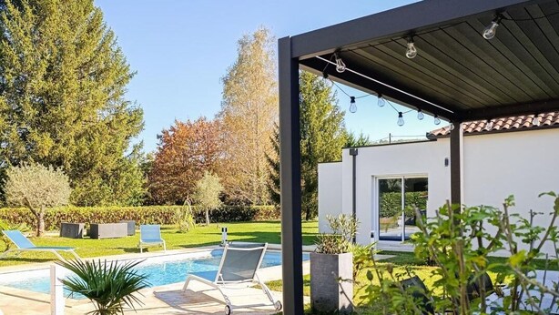 A modern outdoor pool area with lounge chairs, a covered patio, and a well-maintained lawn.