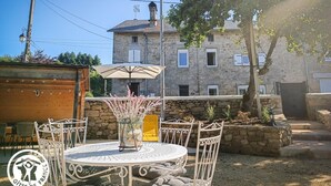 An outdoor dining area with a round table and chairs, a potted plant, and a stone wall. - Gîtes de France® - La Pèira (LATRONQUIERE)
