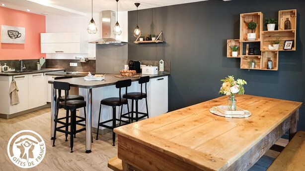 A modern kitchen with a central island, bar stools, pendant lighting, and wooden shelves. - Gîtes de France® - La Pèira (LATRONQUIERE)