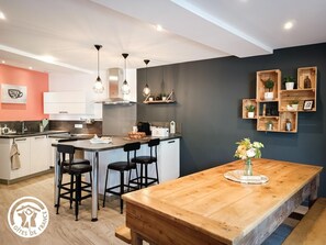A modern kitchen with a central island, bar stools, pendant lighting, and wooden shelves. - Gîtes de France® - La Pèira (LATRONQUIERE)