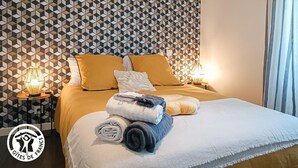 A neatly made bed with a geometric patterned wall behind it, two bedside lamps, and a logo on the wall. - Gîtes de France® - La Pèira (LATRONQUIERE)