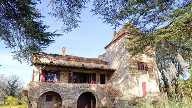 Un edificio de piedra con techo de tejas, dos arcos de entrada y una puerta roja.