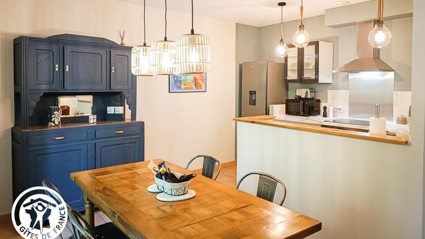 Une cuisine moderne avec des meubles de couleur bleu foncé, une table à manger en bois et des luminaires suspendus.