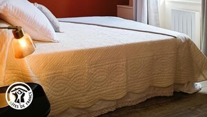 Une chambre à coucher avec un lit, un luminaire suspendu et une fenêtre avec des rideaux.