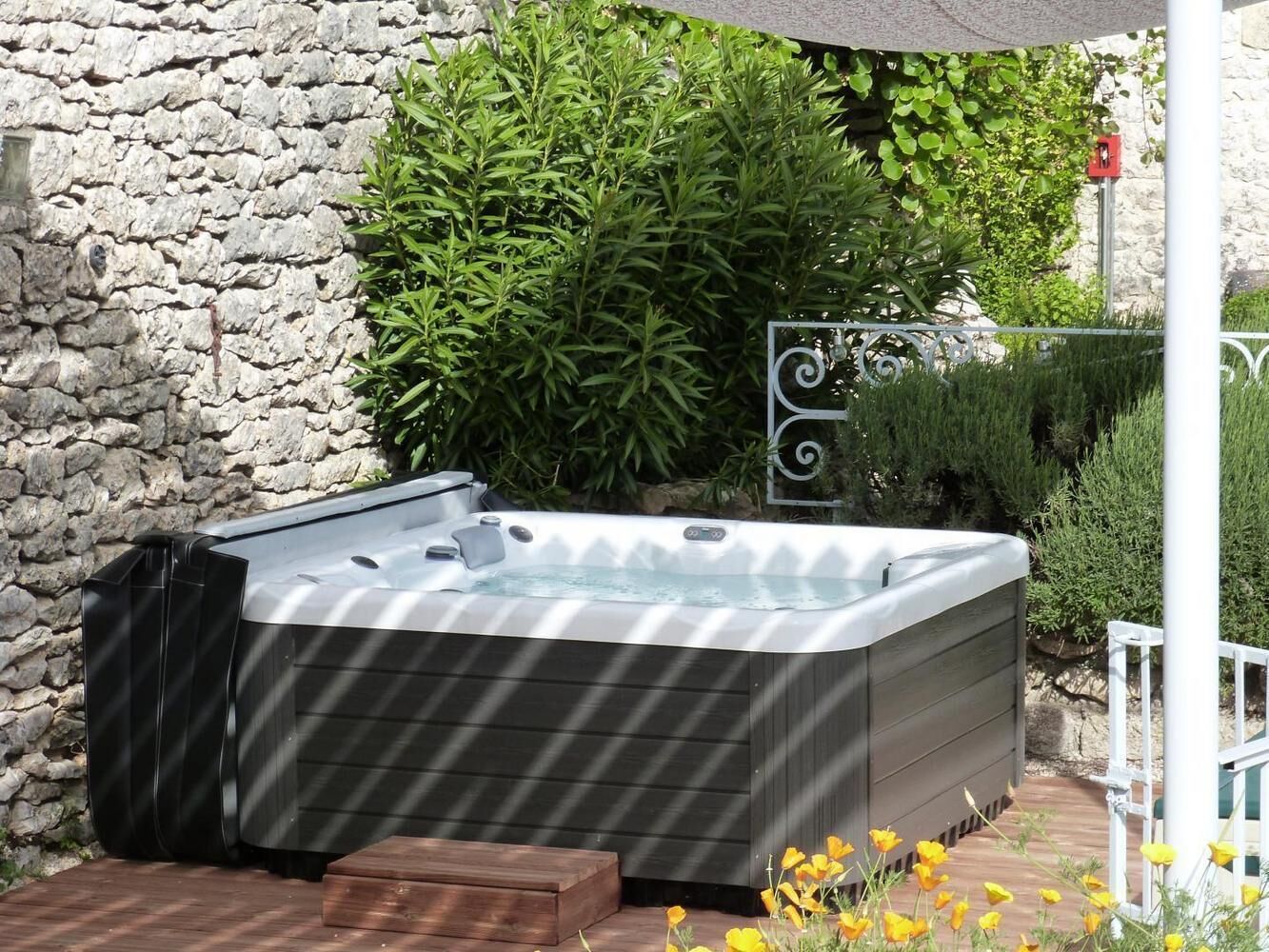 A hot tub in an outdoor setting with a stone wall and greenery in the background.