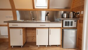 A compact kitchen with a microwave, toaster, and sink. It has wooden cabinets and a window above the sink. - Family En-suite Cabin in South Pembrokeshire (Tenby)