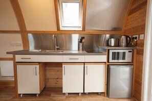 A compact kitchen with a microwave, toaster, and sink. It has wooden cabinets and a window above the sink. - Family En-suite Cabin in South Pembrokeshire (Tenby)