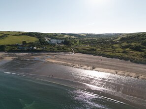 A coastal landscape with a beach, rolling hills, and a small settlement with houses.