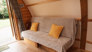 A cozy, wooden-framed room with a sofa bed, two pillows, and a fire extinguisher. - Cosy En-suite Wigwam Glamping Pod (Tenby)