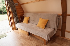 A cozy, wooden-framed room with a sofa bed, two pillows, and a fire extinguisher.