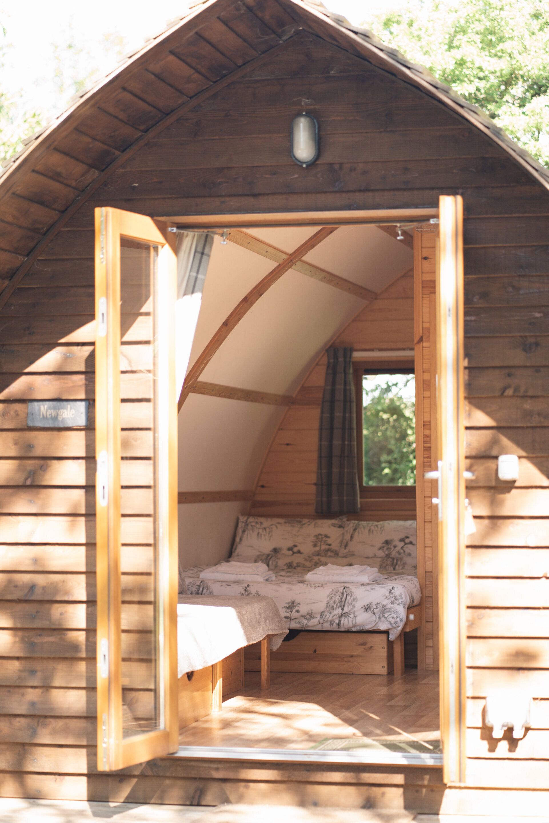 Una cabaña de madera con un altillo, un ventanal pequeño y una puerta que da al exterior.