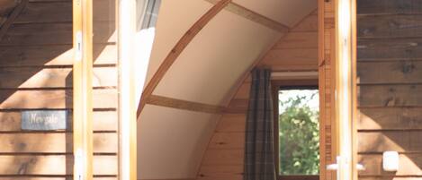 A wooden cabin with a loft bedroom, a small window, and a door leading outside.