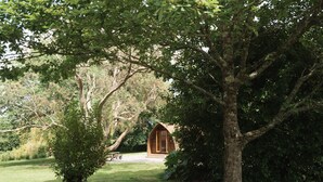 A rustic wooden cabin nestled in a lush, green landscape with a picnic table nearby. - Cosy En-suite Wigwam Glamping Pod (Tenby)