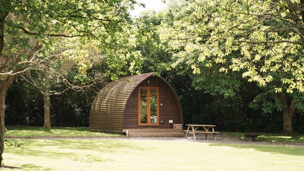 A small wooden cabin with a porch, surrounded by trees. - Cosy En-suite Wigwam Glamping Pod (Tenby)