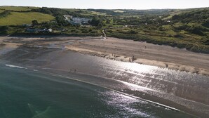 A coastal landscape with a beach, rolling hills, and a small settlement with houses. - Cosy En-suite Wigwam Glamping Pod (Tenby)