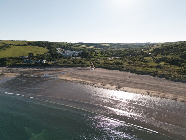 A coastal landscape with a beach, rolling hills, and a small settlement with houses.