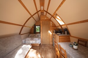 A cozy attic bedroom with a bed, a sofa, a small kitchenette, and a dining area.