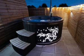 Een hottub met een sterren- en vlamdesign, omringd door houten terrassen en een houten hek.