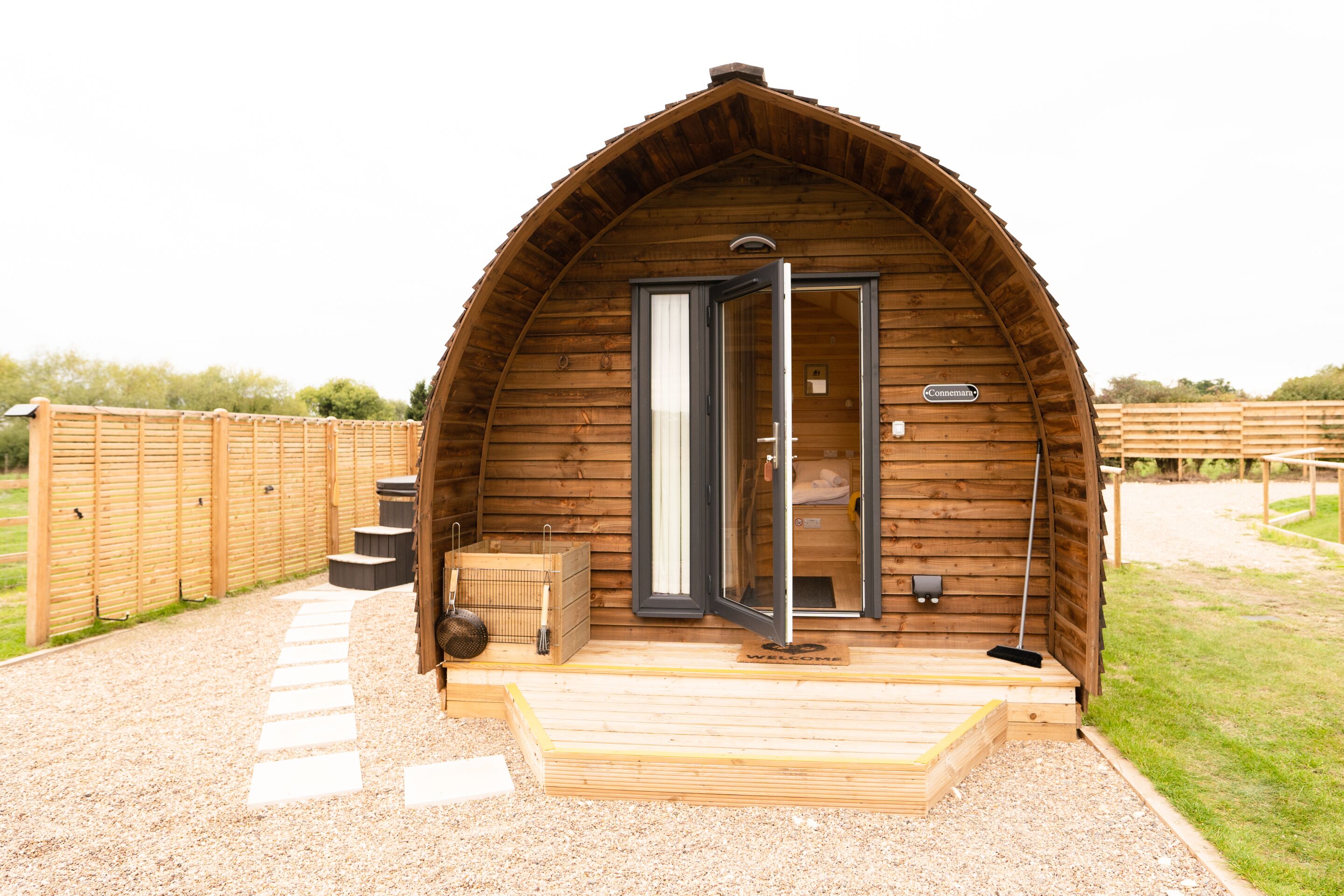 A wooden cabin with a curved roof, a wooden deck, and a gravel pathway leading to the entrance.