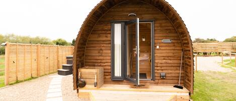 A wooden cabin with a curved roof, a wooden deck, and a gravel pathway leading to the entrance.