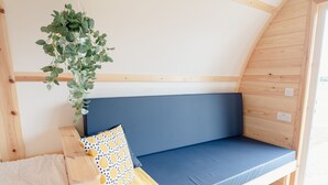 A cozy, wooden interior with a blue cushioned bench, a hanging plant, and a patterned pillow.