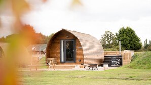 A wooden cabin with a curved roof, a door, and a small outdoor seating area.