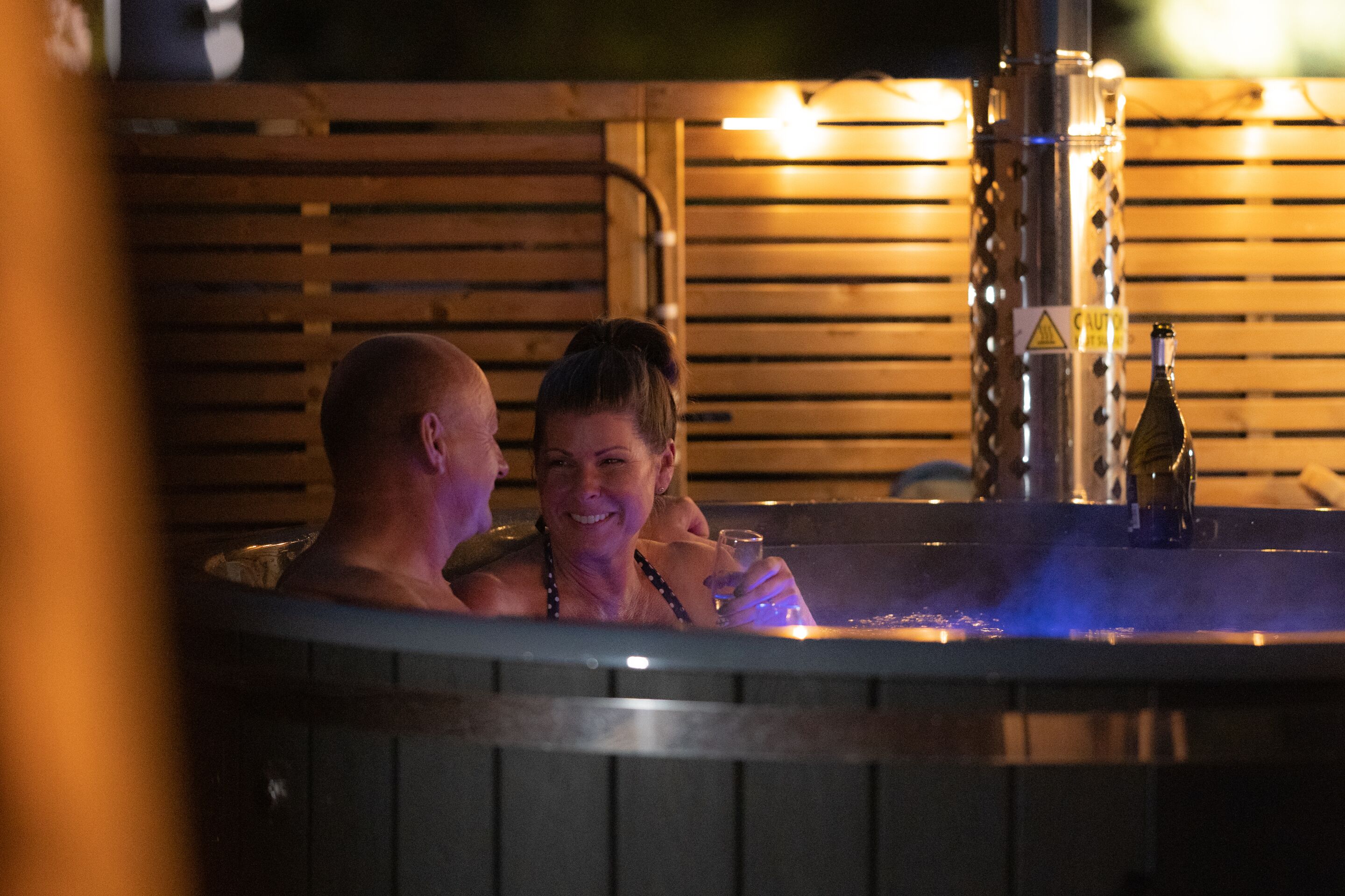 A hot tub with wooden slats and a bottle of wine.