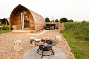 A wooden cabin with an open door, a fire pit, and a wooden deck.