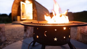 A circular outdoor grill with star and moon designs, positioned in front of a wooden building with an open door.