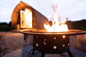 Ein runder Grill für den Außenbereich mit Stern- und Mondmotiven, vor einem Holzhaus mit offener Tür platziert.