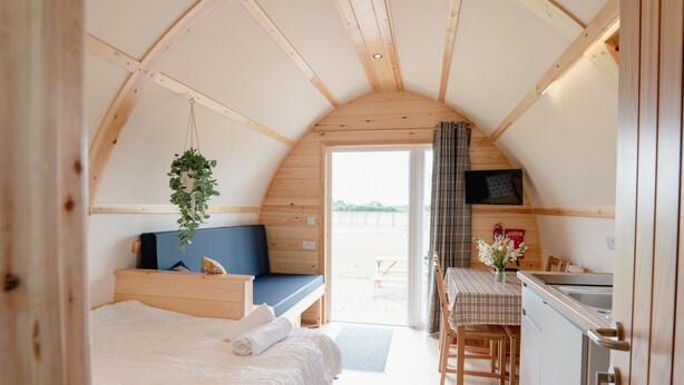 A cozy, compact room with a bed, a small seating area, a kitchenette, and a view through a door.