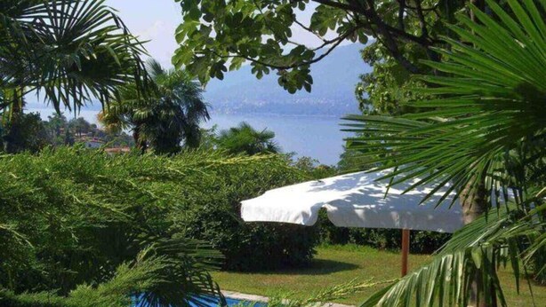 A swimming pool surrounded by lush greenery and a white umbrella providing shade. - Mirabella villa with pool and garden  in Brezzo di (Brezzo di Bedero)