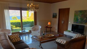 A living room with a sofa, armchairs, a coffee table, a TV, and a view of greenery outside. - Mirabella villa with pool and garden  in Brezzo di (Brezzo di Bedero)