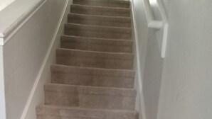 Een betegeld trappenhuis met witte leuningen en een witte muur.
