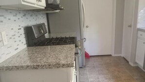 Een keuken met een granieten aanrecht, witte kasten, een fornuis en een koelkast.