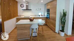 Een moderne keuken met houten kastjes, een centraal eiland en een eethoek met twee barkrukken.