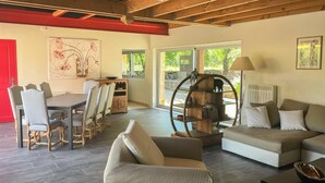 A spacious living area with a dining table, chairs, a sofa, and a unique circular wooden shelf.