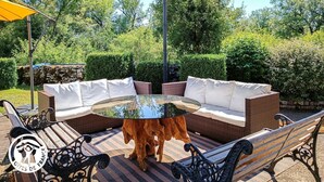 An outdoor seating area with a round glass table, wicker sofa, and metal chairs.
