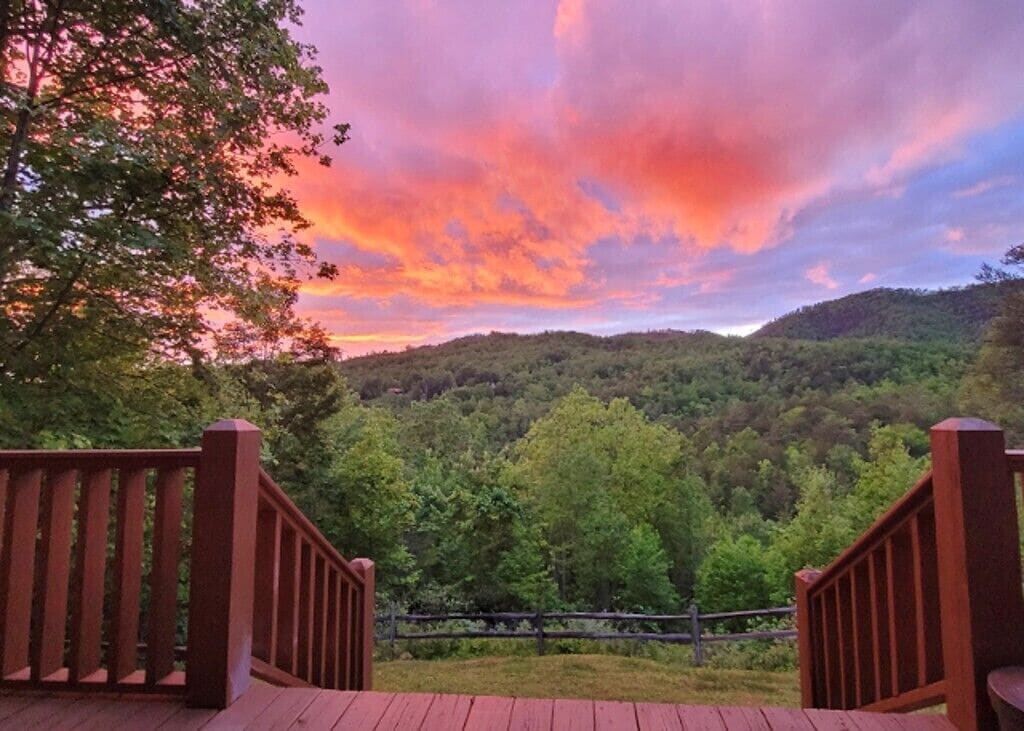 A wooden deck with a view of a forested hill under a colorful sky.