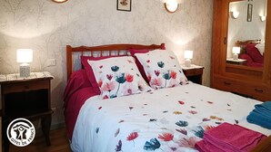 Un dormitorio con estructura de cama de madera, ropa de cama floral, dos lámparas de noche, una mesita de noche, un espejo y un papel tapiz con estampado floral.