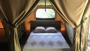 Ein Bett mit einem gemusterten Überwurf, Vorhängen und einem Fenster mit Blick auf Grünflächen.
