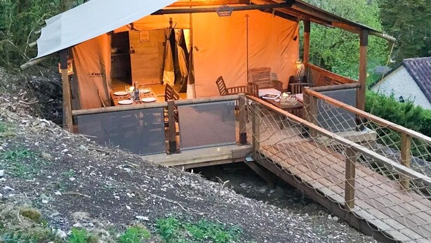 Ein rustikales Zelt mit einer Holzterrasse und einer Seilleiter, die zum Eingang führt.