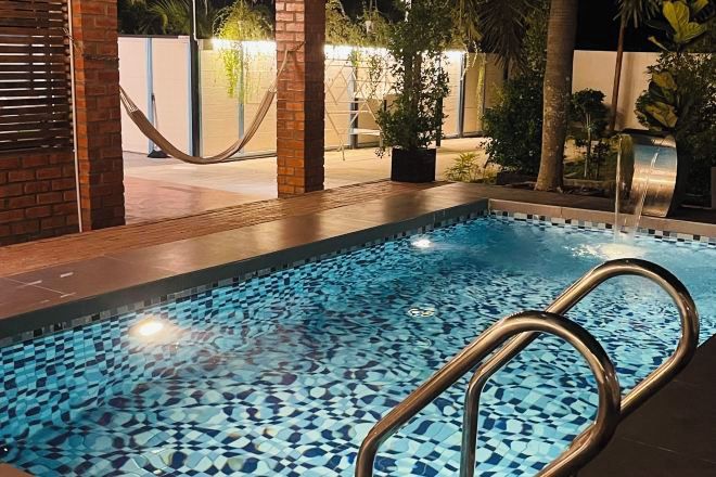 A swimming pool with a mosaic tile design, surrounded by plants and a brick wall.