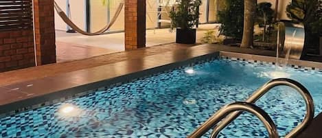 Una piscina con diseño de mosaicos, rodeada de plantas y un muro de ladrillo.