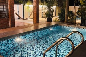 Una piscina con diseño de mosaicos, rodeada de plantas y un muro de ladrillo.