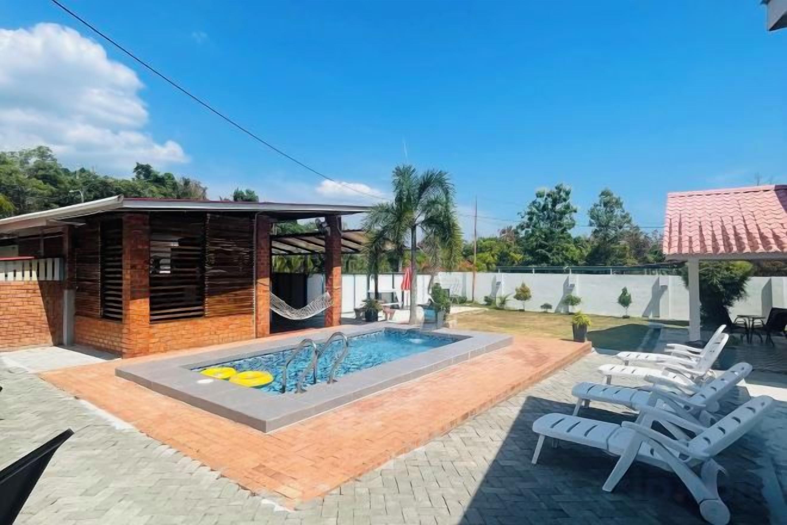 A swimming pool with lounge chairs, a covered seating area, and a brick patio.
