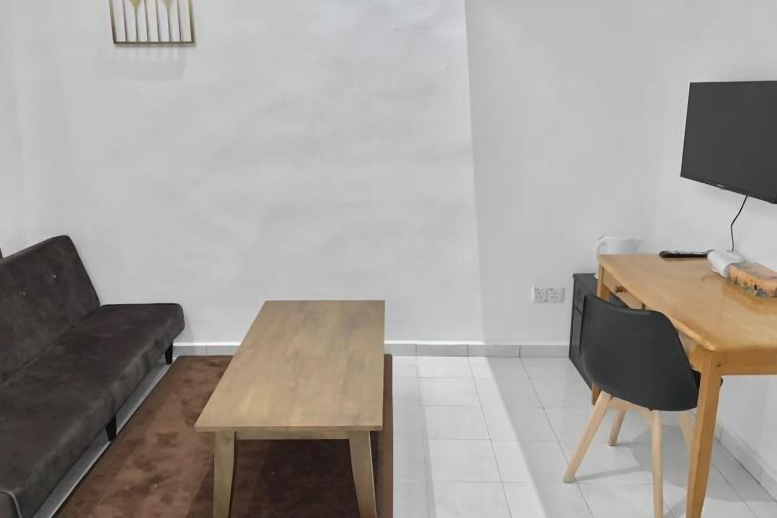 Een moderne woonkamer met een donkergrijze bank, een houten salontafel, een eettafel met stoelen en een flatscreen televisie aan de muur.