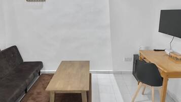 Een moderne woonkamer met een donkergrijze bank, een houten salontafel, een eettafel met stoelen en een flatscreen televisie aan de muur.