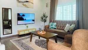 A modern living room with a large flat-screen TV, a brown sofa, a wooden coffee table, and a patterned rug. - Rooma Kichi Private Pool (Langkawi)